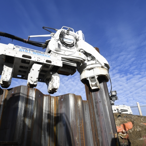 steel piling going into ground with man in Hi-vis stood on the right hand side