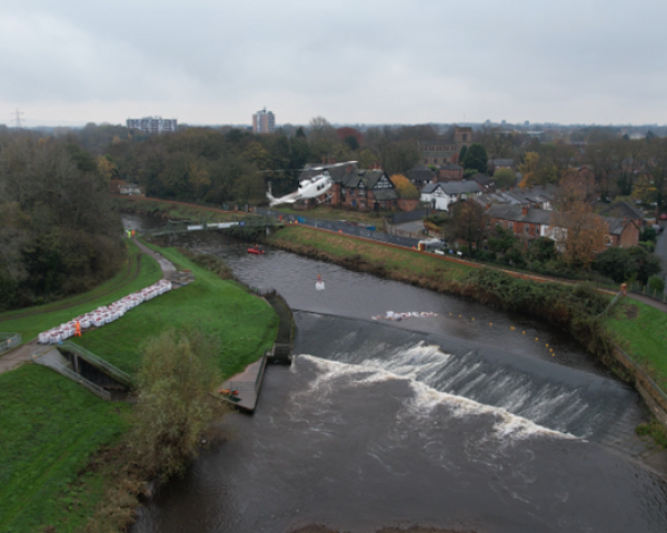 Picture of a helicopter carrying a bulk bag over a river.